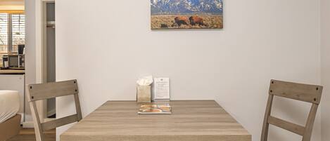 Zona pranzo con tavolo e sedie in legno, un quadro al muro e una cucina sullo sfondo.