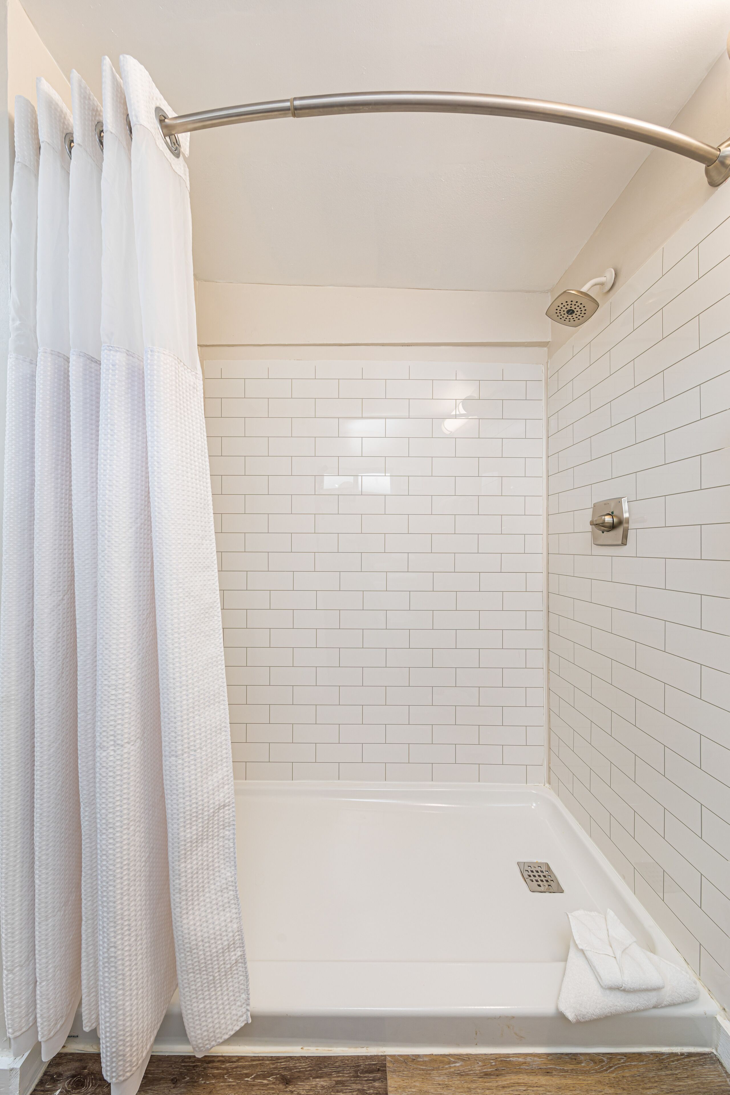 A shower area with a white tiled wall, a showerhead, and a curtain.