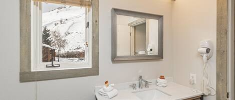 A bathroom with a white sink, wooden vanity, a mirror, a hairdryer, and a window with a view of a snowy landscape.