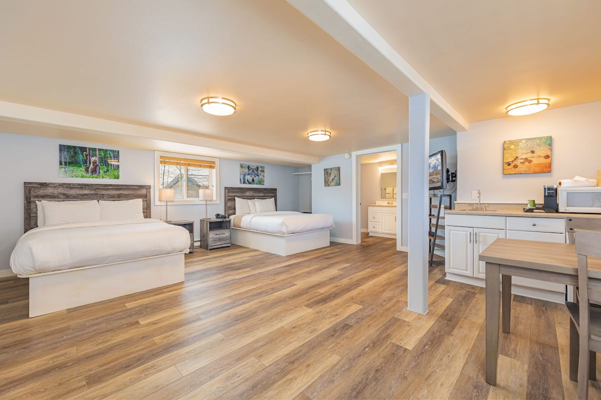 A spacious bedroom with two beds, a wooden floor, and a kitchenette area with a microwave and sink.