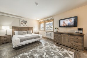 A bedroom with a bed, bedside tables, a TV, and a window with a view. - Miller Park Lodge (Jackson)