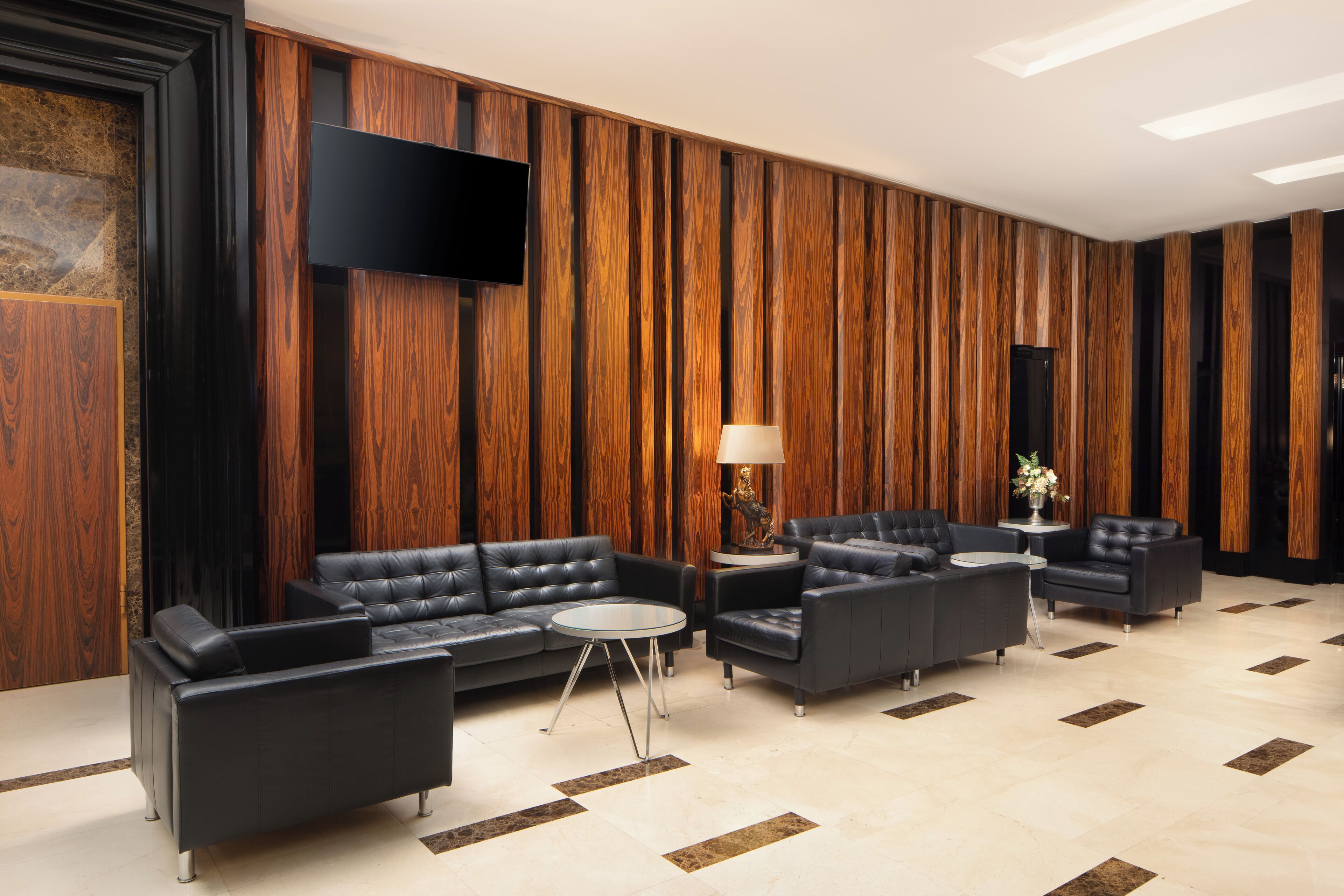A modern lobby with leather sofas, a flat-screen TV, and a wooden panel wall.