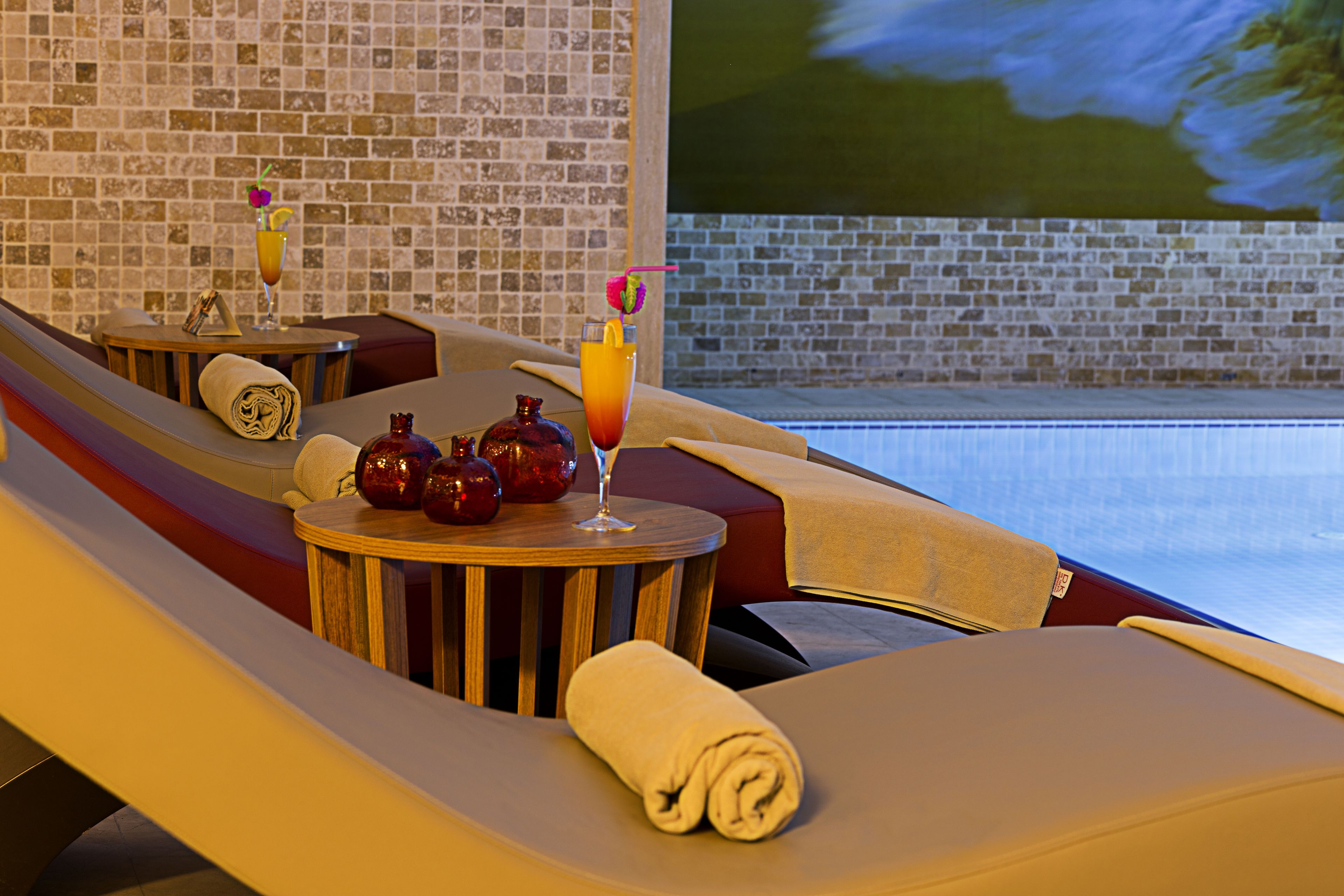 A sun lounge with a brick wall, a pool view, and a table with a drink and decorative items.