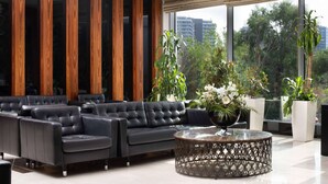 Un salon moderne avec un ensemble de canapés en cuir noir, une table basse ronde et de grandes fenêtres donnant sur un paysage verdoyant et des bâtiments.