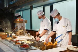 Des chefs préparent des plats dans une cuisine professionnelle dotée de surfaces en acier inoxydable et de divers ustensiles de cuisine.