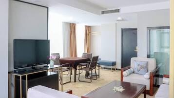 A hotel room with a flat-screen TV, a dining table with chairs, a sofa, a coffee table, and a window with curtains.