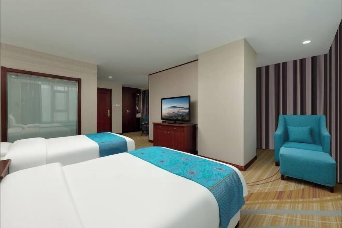 Ein Hotelzimmer mit zwei Betten, einem Fernseher, einem Schreibtisch und einem Stuhl.