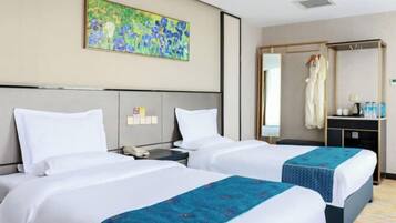 A hotel room with two beds, a painting on the wall, a mirror, and a small table with toiletries.