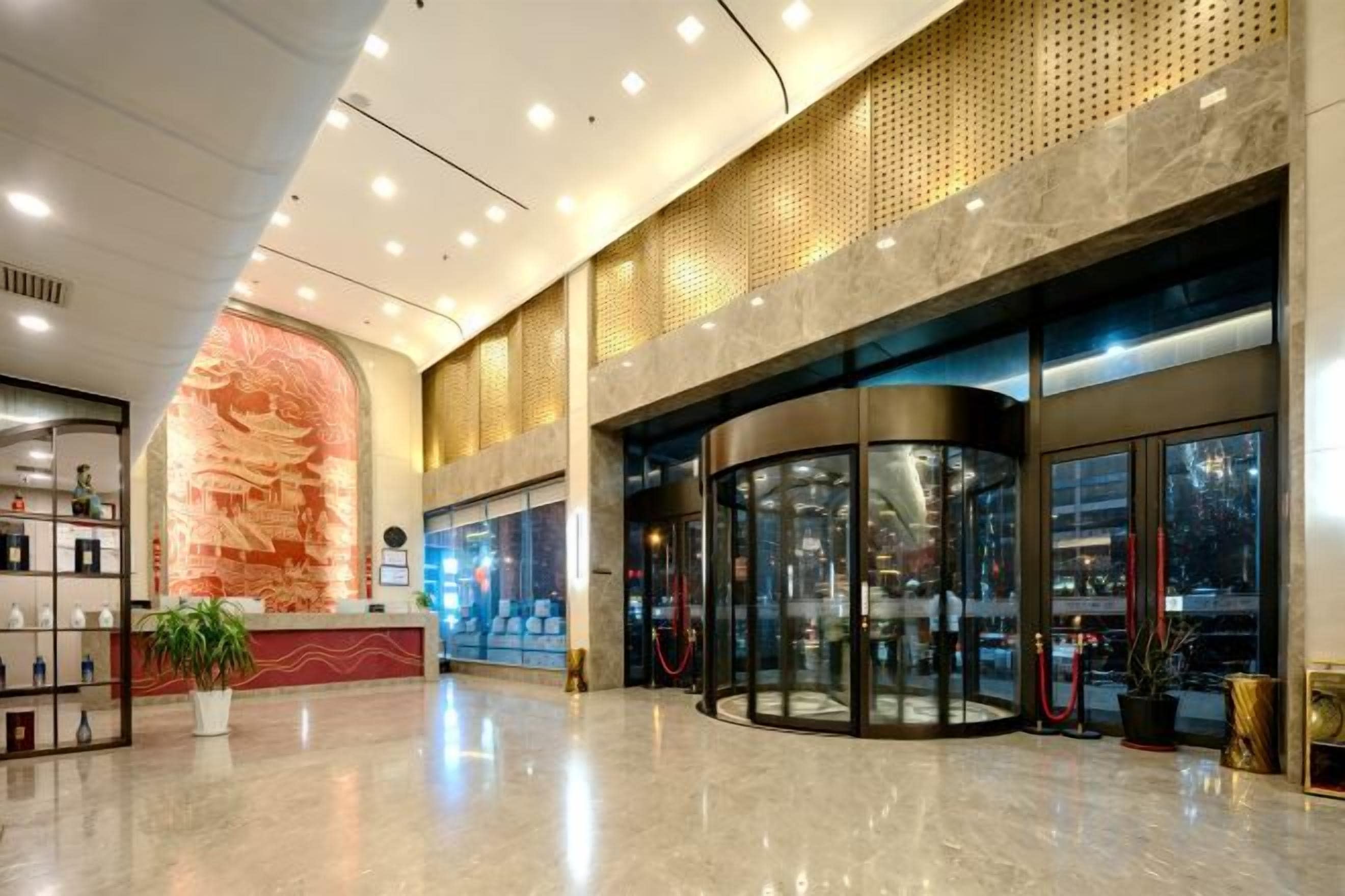 A hotel lobby with a reception desk, a large decorative wall, and a revolving door.