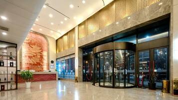A hotel lobby with a reception desk, a large decorative wall, and a revolving door.