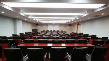 A conference room with rows of tables and chairs, a projector screen, and a whiteboard.
