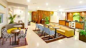 A modern hotel lobby with a reception desk, seating area with sofas and chairs, and decorative plants. - Hilton Garden Inn Queretaro (Querétaro)