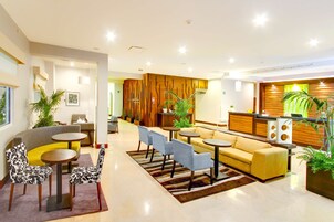 Un moderno vestíbulo de hotel con mostrador de recepción, zona de estar con sofás y sillones, y plantas decorativas.