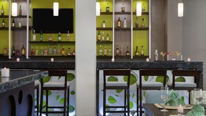 A bar area with multiple shelves of liquor bottles, bar stools, and a television screen. - Hilton Garden Inn Queretaro (Querétaro)