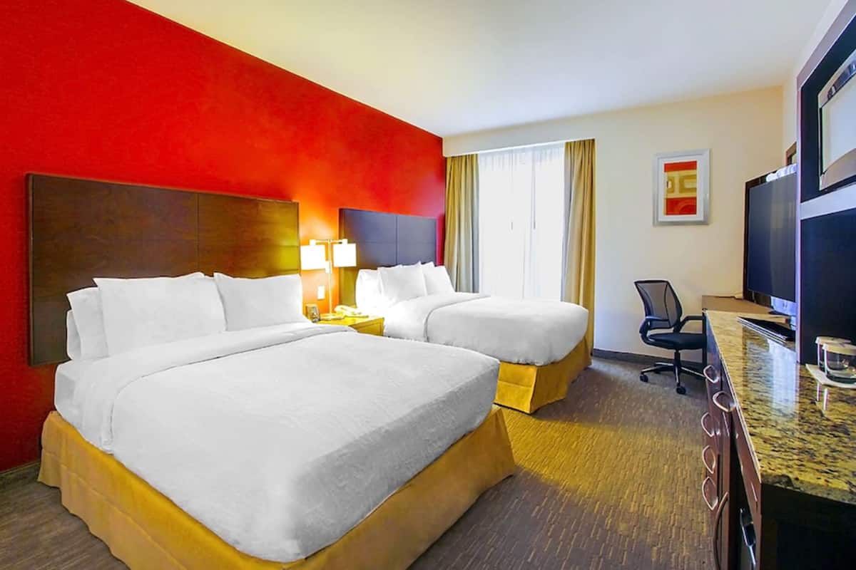 A hotel room with two beds, a desk, a chair, a television, and a window with curtains.