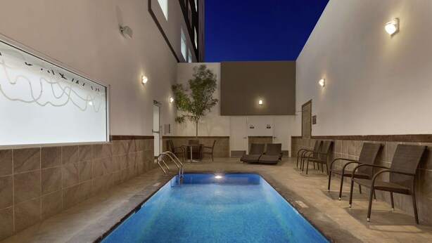 A swimming pool with a tiled deck, lounge chairs, and a wall-mounted light fixture. - Hilton Garden Inn Queretaro (Querétaro)