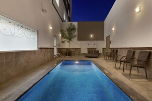 Una piscina con solárium empinado, sillas de descanso y una lámpara fijada a la pared.