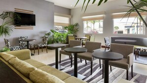 A modern lobby with a sofa, chairs, tables, a TV, and large windows with a view of the street. - Hilton Garden Inn Queretaro (Querétaro)