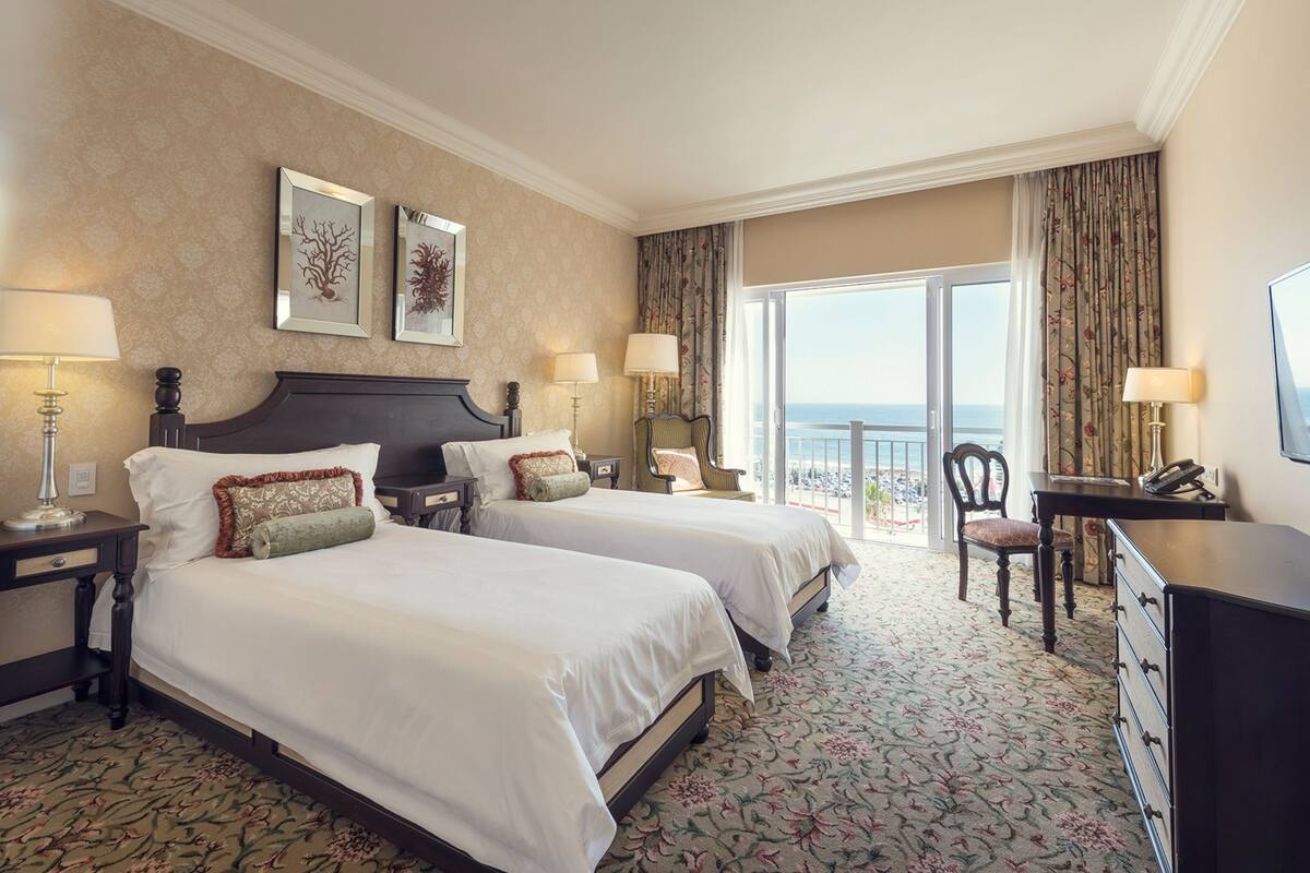 Habitación de hotel con dos camas, un escritorio, una silla y un balcón con vista a la playa.