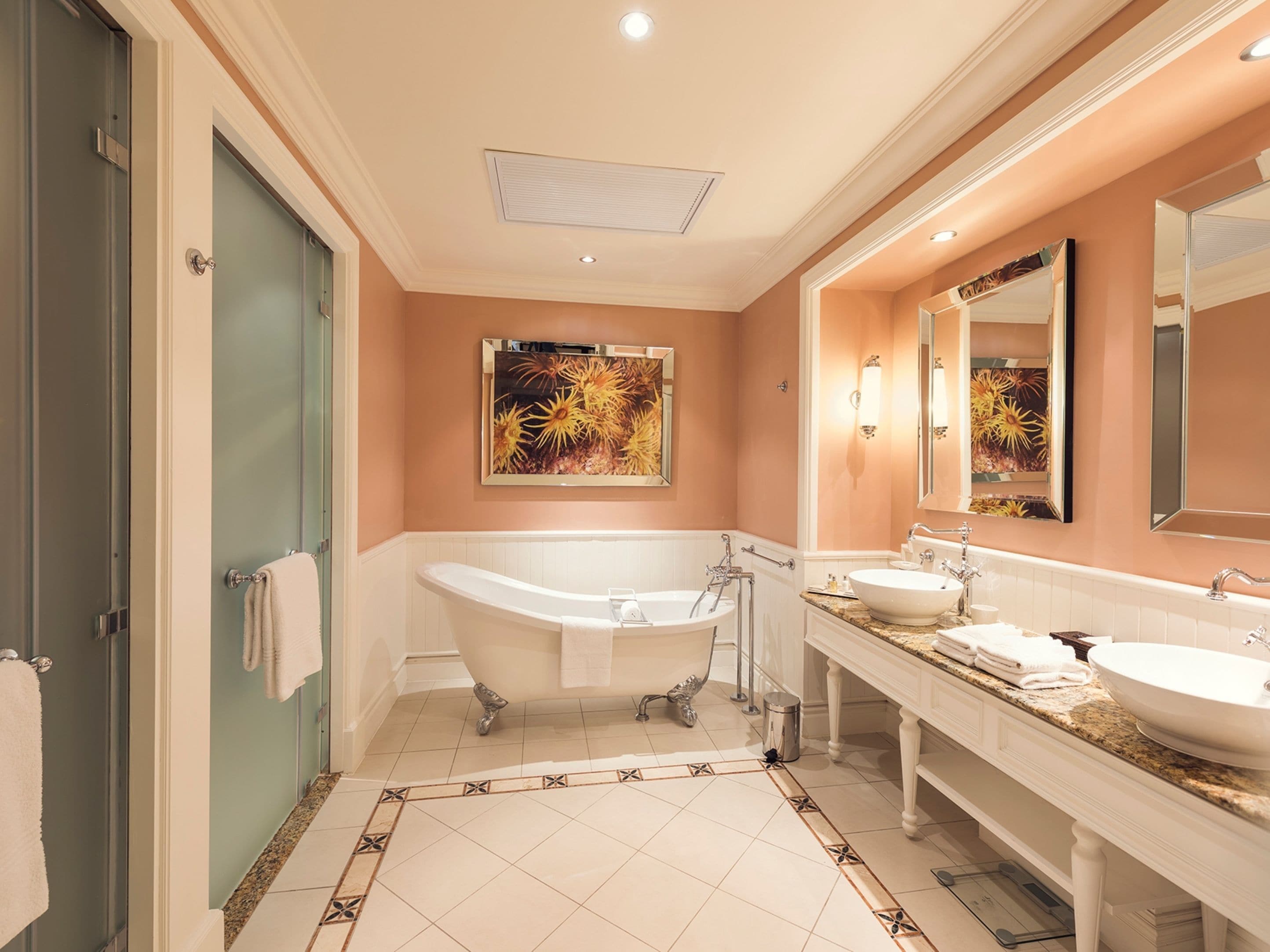 A bathroom with a freestanding bathtub, two sinks, a large mirror, and a decorative wall piece.