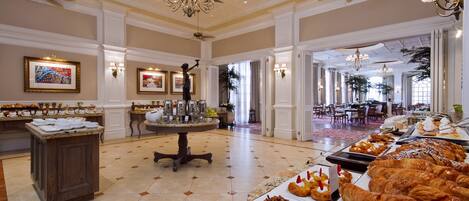 Um amplo saguão de hotel com área de buffet, oferecendo doces e um espaço para café.