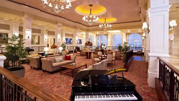 Un'imponente hall con un pianoforte a coda, comodi posti a sedere, lampadari e ampie finestre.
