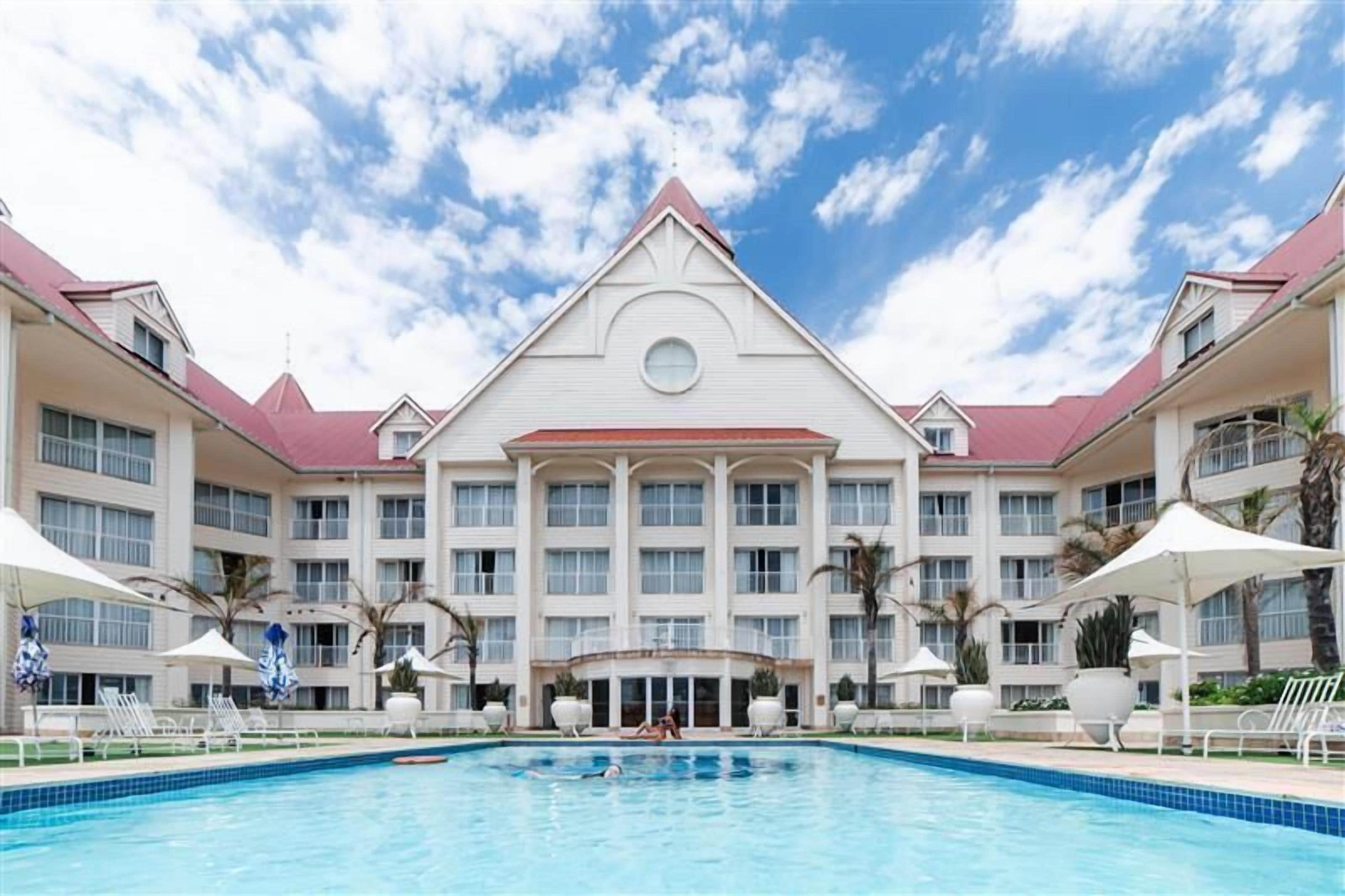 A hotel with a large pool, multiple balconies, and a symmetrical facade.