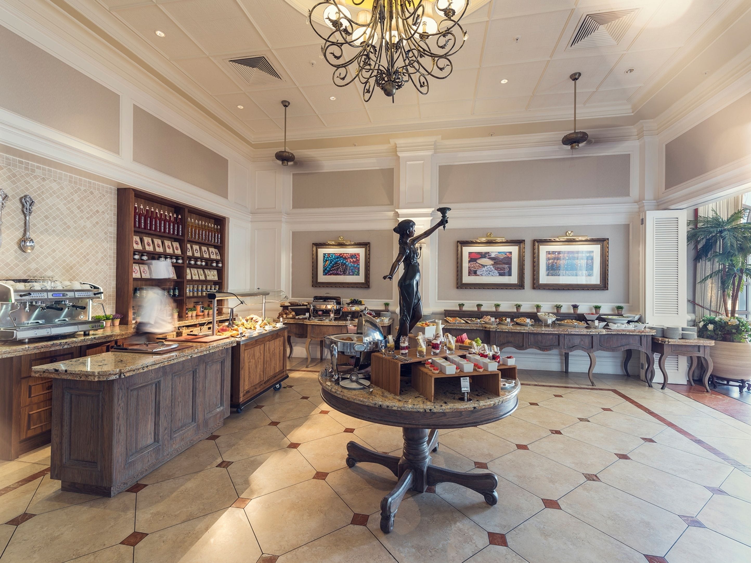 A spacious hotel lobby with a central round table, a coffee station, and a statue.