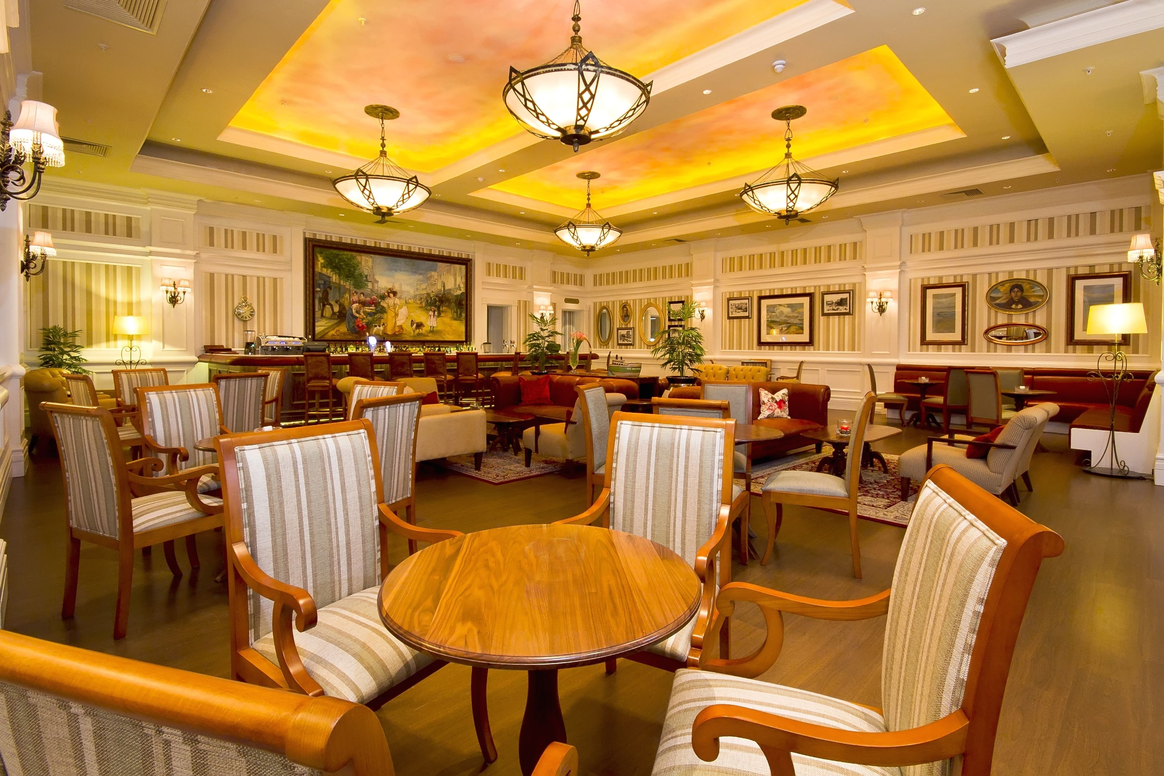 A spacious hotel lobby with multiple seating areas, chandeliers, and framed artwork on the walls.