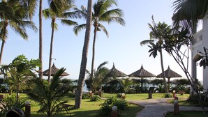 A tropical resort with palm trees, a pathway, and thatched-roof structures. - MUINE SUN & SEA BEACH ( BOUTIQUE RESORT & GLAMPING) (Mui Ne)