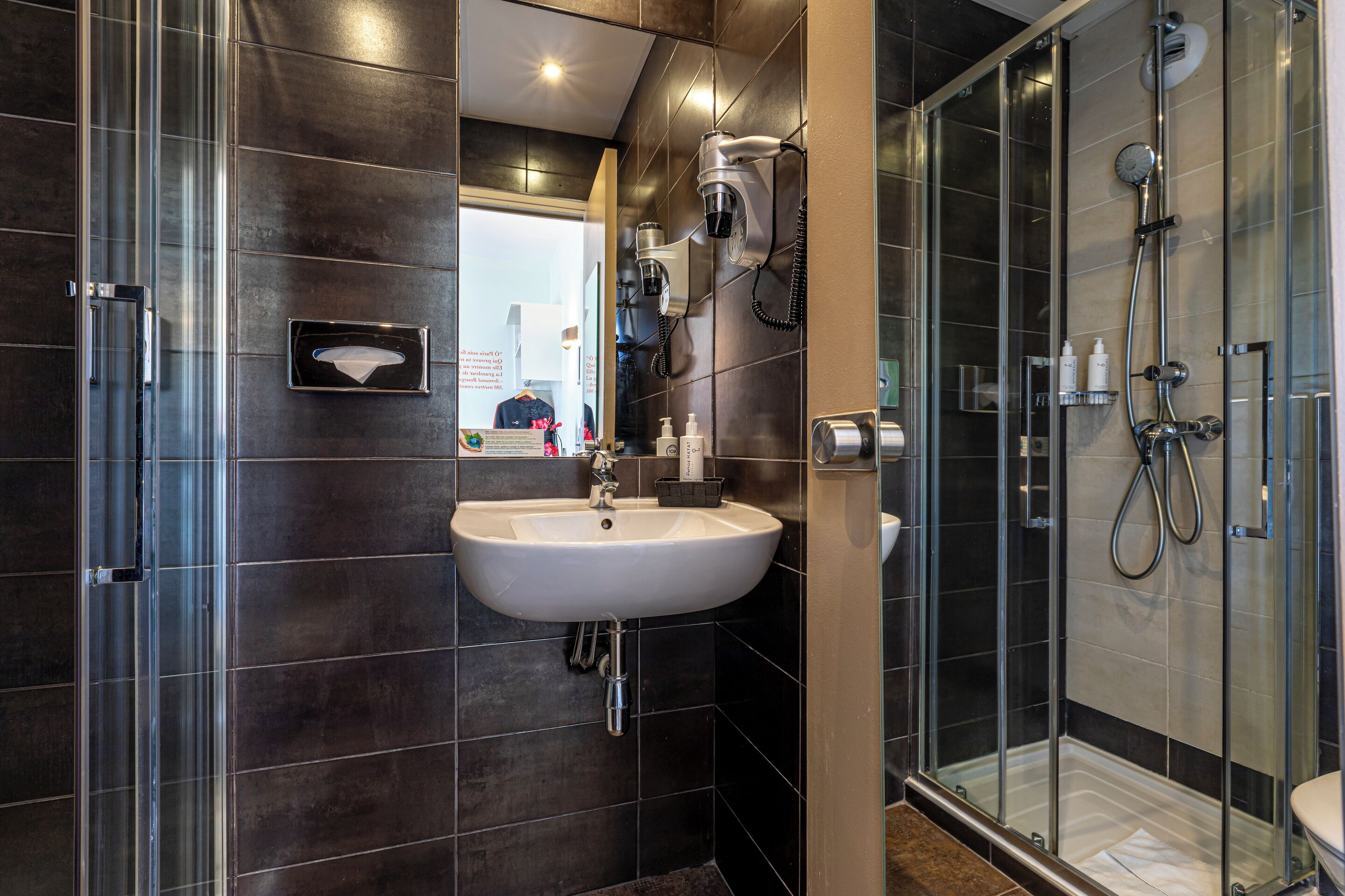 Une salle de bain moderne avec une douche à parois de verre, un lavabo avec un miroir et un sèche-cheveux fixé au mur.