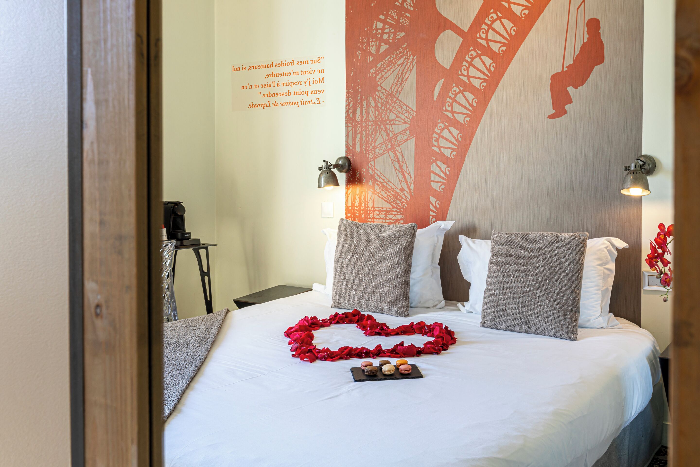 A hotel room with a bed, pillows, a heart-shaped decoration, and a wall with a silhouette of a bridge.