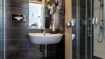 Un bagno moderno con piastrelle scure, un lavandino bianco e un box doccia in vetro.