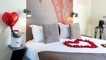 Ein Hotelzimmer mit einem Bett, Kissen, einem Nachttisch mit Champagnerflasche und Gläsern sowie einem dekorativen Herzballon.