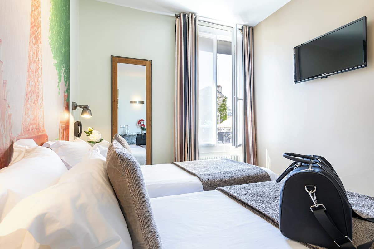 A hotel room with two beds, a flat-screen TV, a mirror, and a window with curtains.