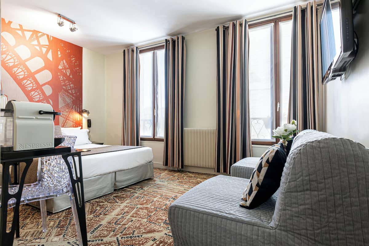 A hotel room with a bed, a desk with a coffee maker, a chair, and a sofa.
