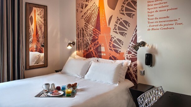 Habitación de hotel con cama, bandeja de desayuno, espejo y una pared con una cita en francés.