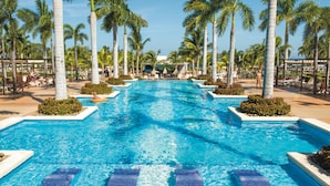 A large pool with clear blue water, surrounded by palm trees and lounge chairs. - Hotel Riu Palace Costa Rica - All Inclusive (Sardinal)