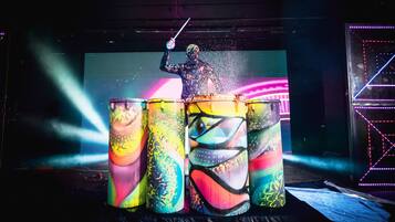 Een persoon bespeelt een drumstel op een podium, met drums in kleurrijke, abstracte verf.