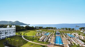 A resort with a large pool, a white building with multiple balconies, and a view of the ocean. - Hotel Riu Palace Costa Rica - All Inclusive (Sardinal)