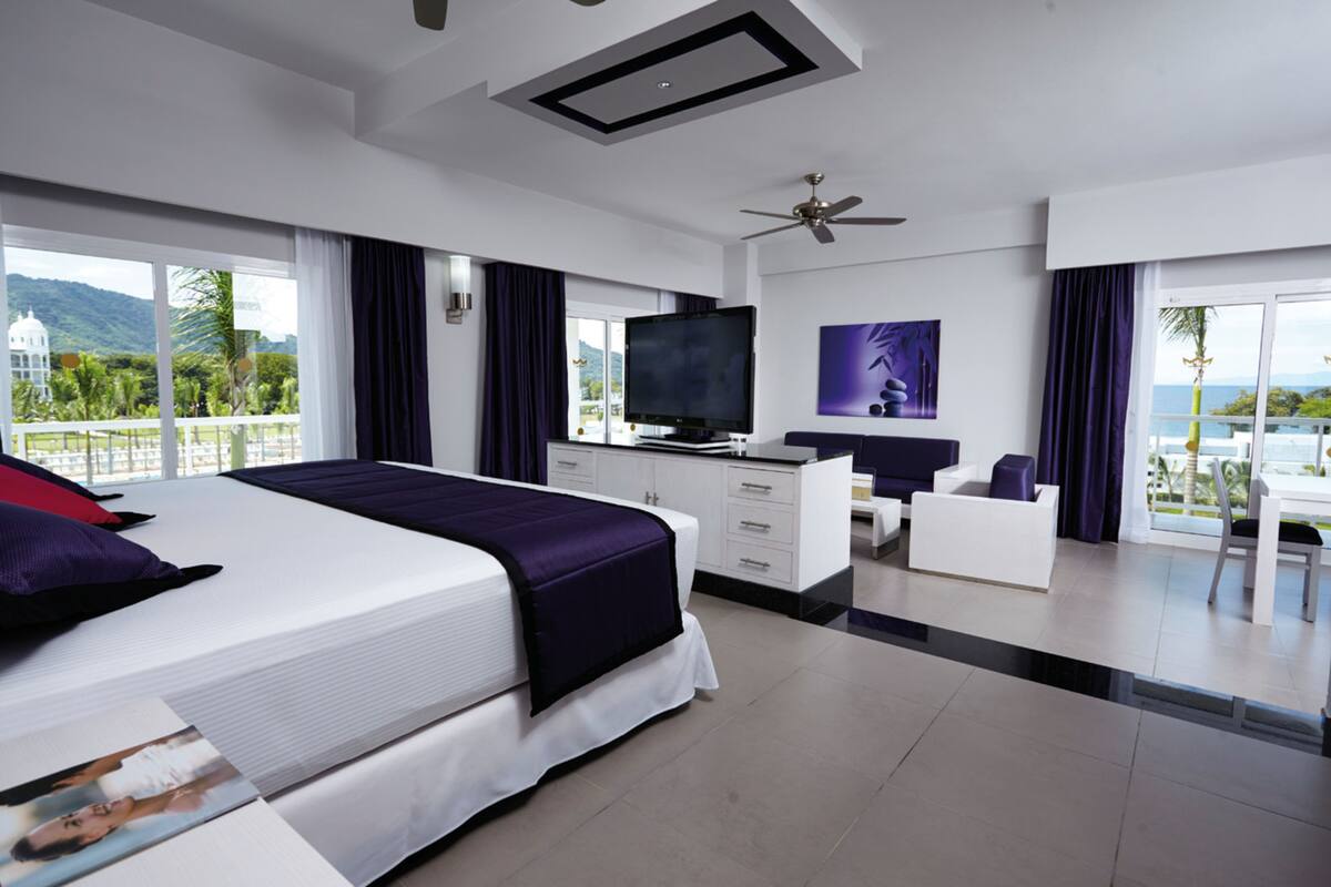 Una habitación de hotel moderna con una cama grande, televisión de pantalla plana, escritorio y balcón con vistas a las montañas.