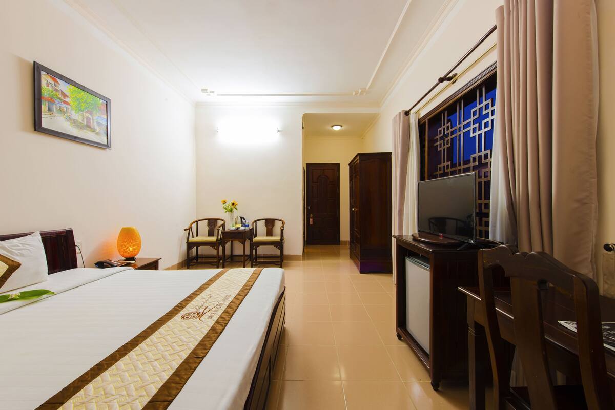 A hotel room with a bed, a desk, a chair, a television, and a door leading to another room.