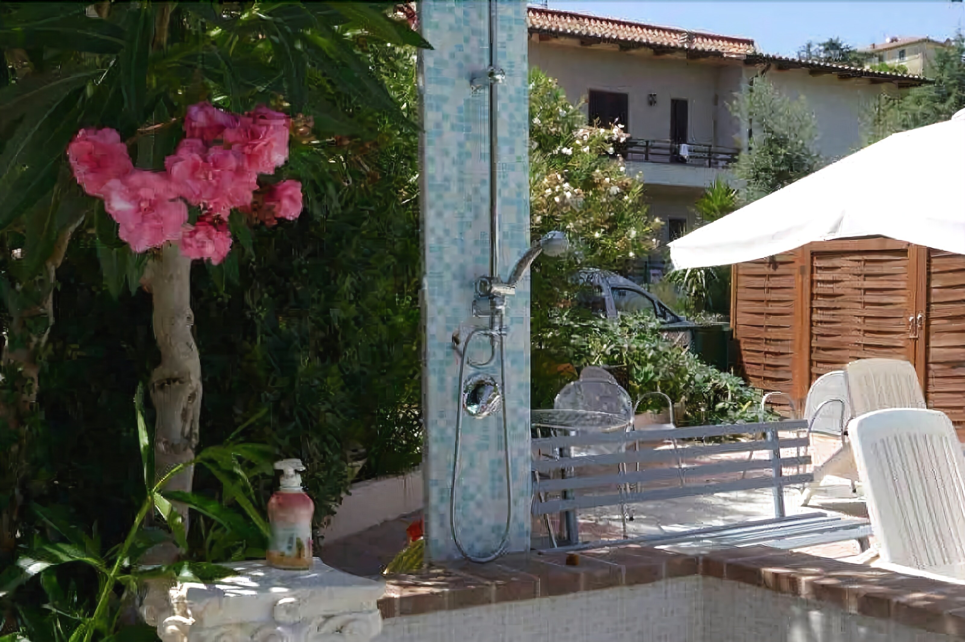 Un espace piscine équipé d’une douche, de chaises blanches et d’un parasol blanc.