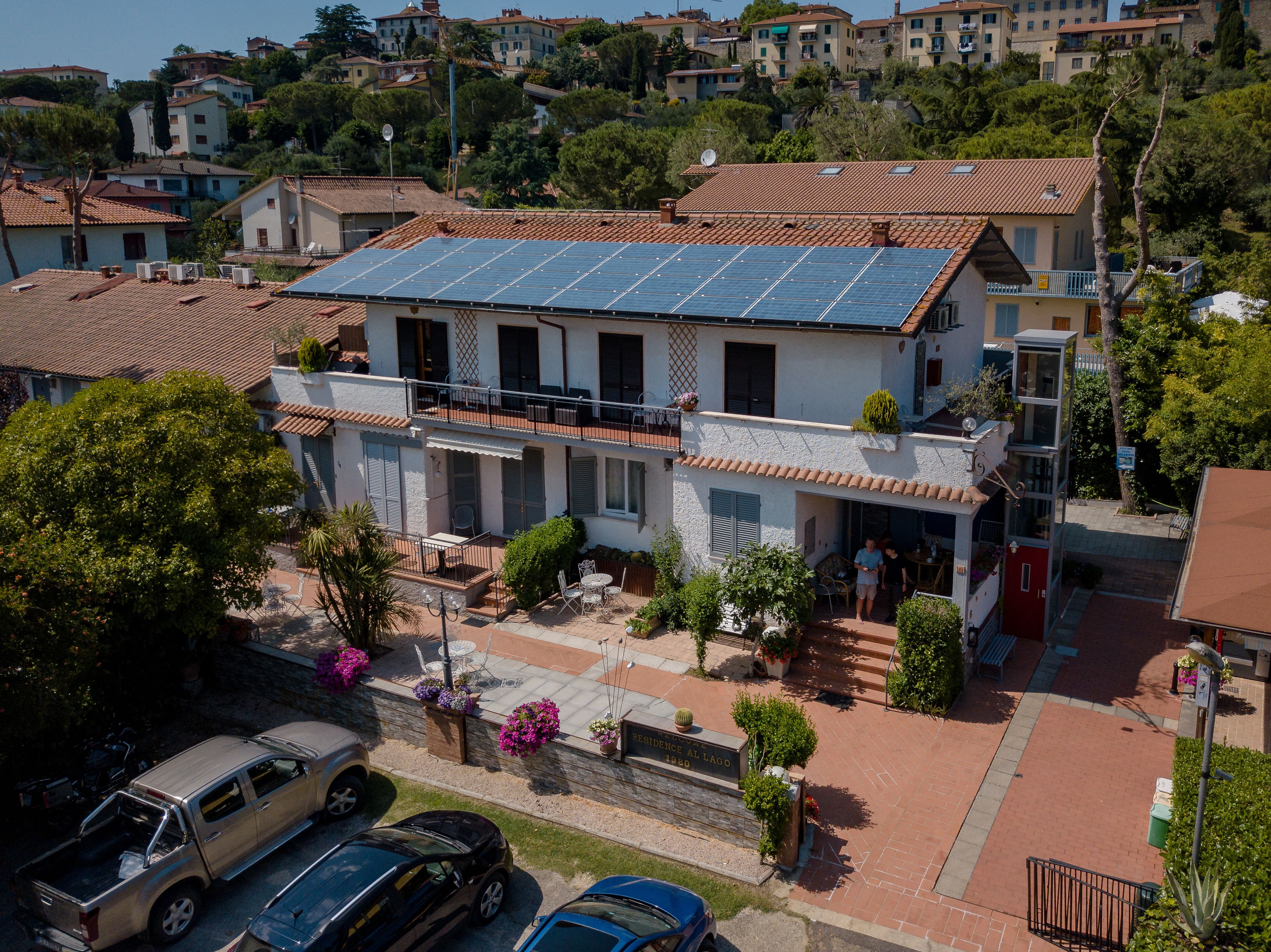 A two-story building with a solar panel roof, a balcony, and a small garden area with potted plants.