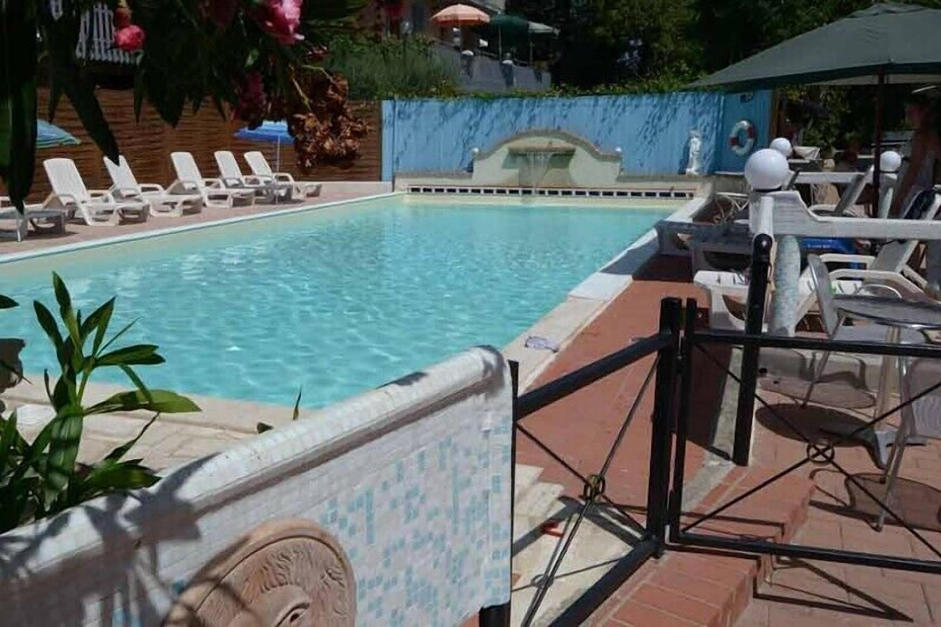 A swimming pool with lounge chairs and umbrellas, surrounded by a brick wall and greenery.