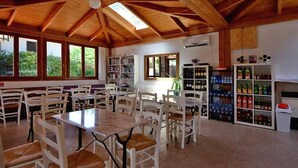 Un espace repas avec des tables et des chaises en bois, une bibliothèque et un réfrig érateur pour les boissons.