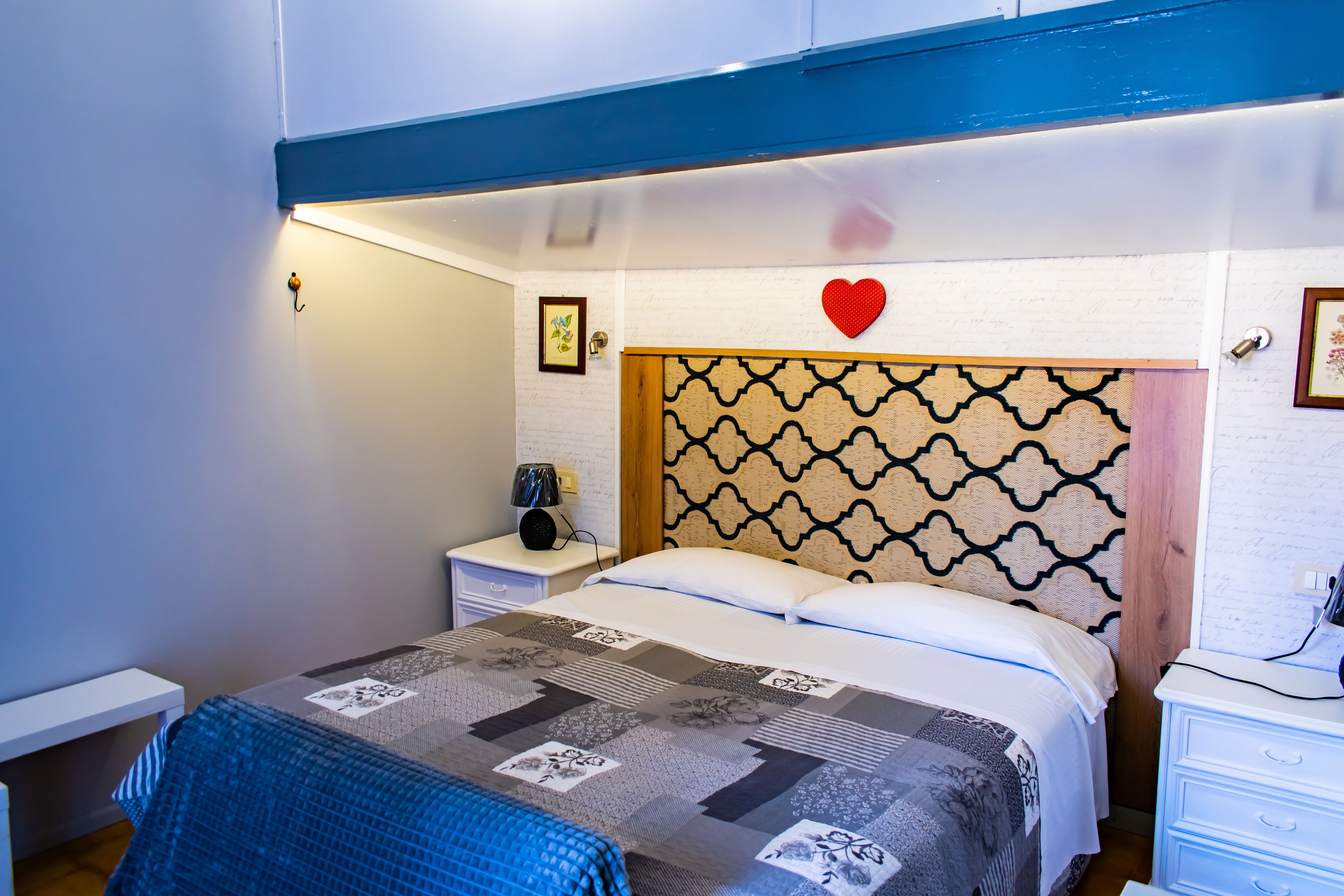 A bedroom with a bed, a nightstand, a dresser, and a wall with a heart decoration.