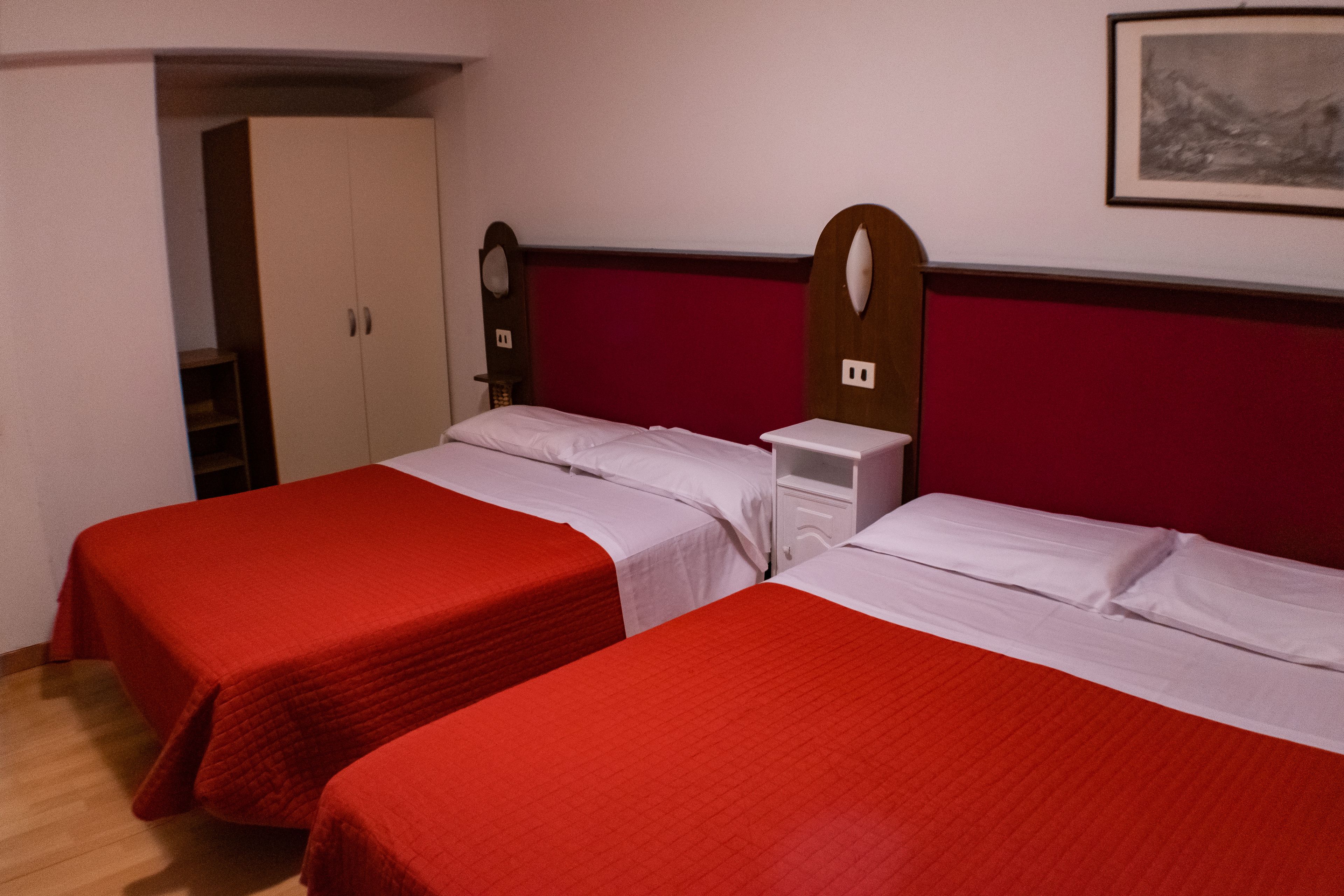 A room with two beds, each with a red bedspread, a wooden headboard, and a white nightstand.