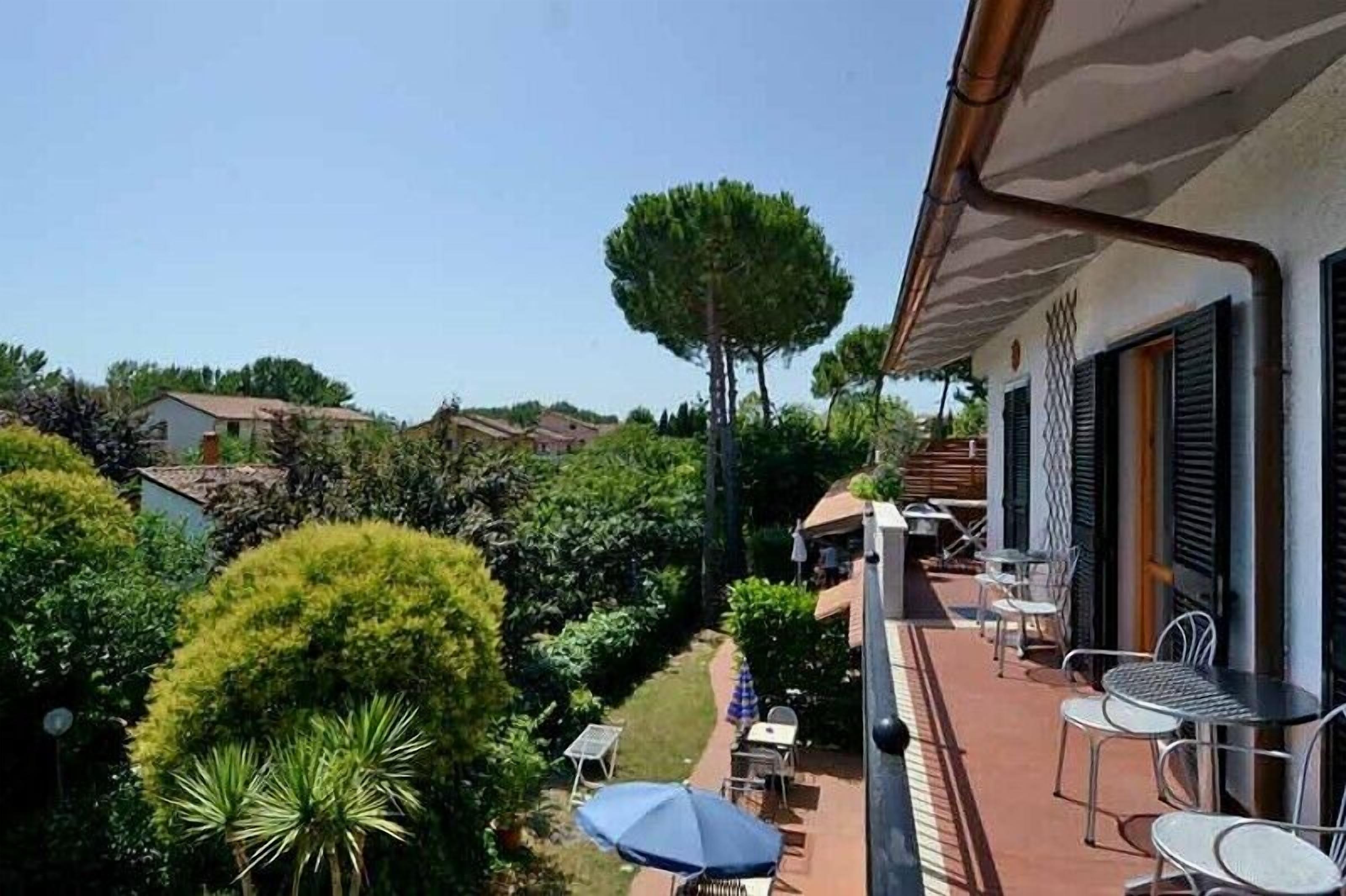 A balcony with outdoor seating, surrounded by lush greenery and a clear sky.