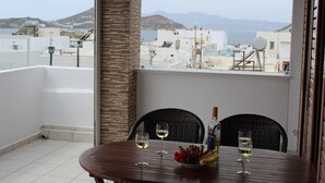 A balcony with a table set for two, two wine glasses, a bottle of wine, and a bowl of snacks.